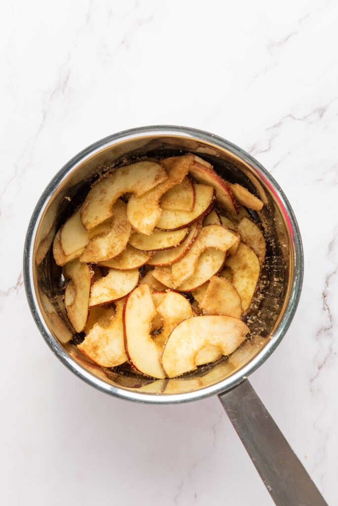 Apple slices coated with sugar and cinnamon in a saucepan, beginning to soften