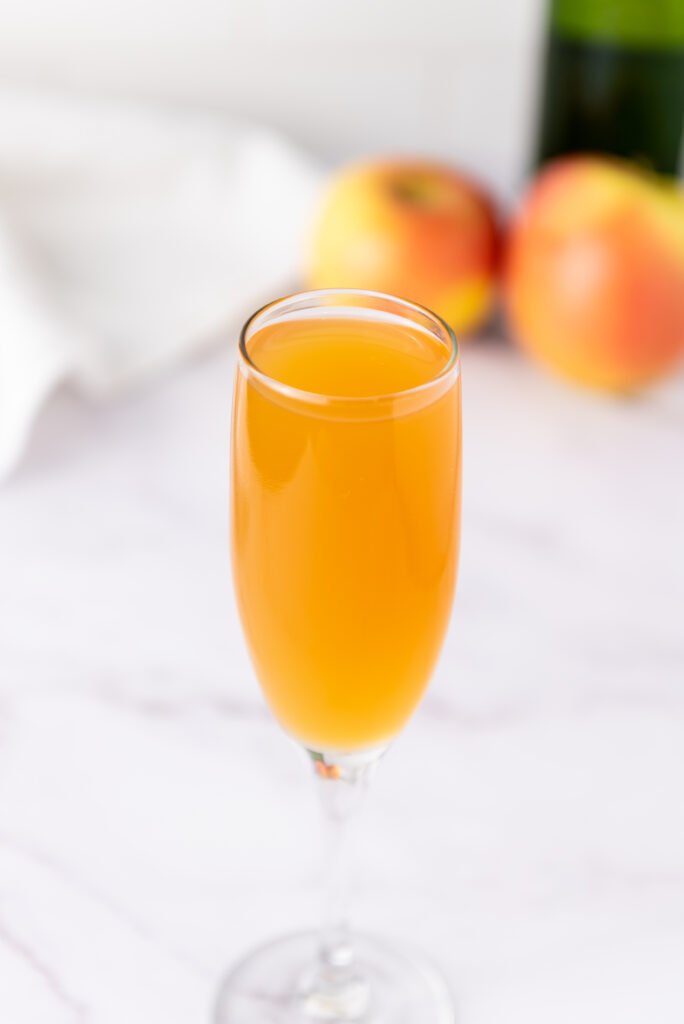 A champagne flute filled with golden apple cider mimosa, with fresh apples blurred in the background