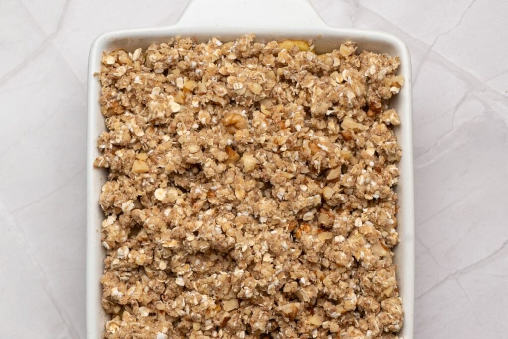 Apple crisp in a baking dish with oat topping spread evenly over the apple filling before baking