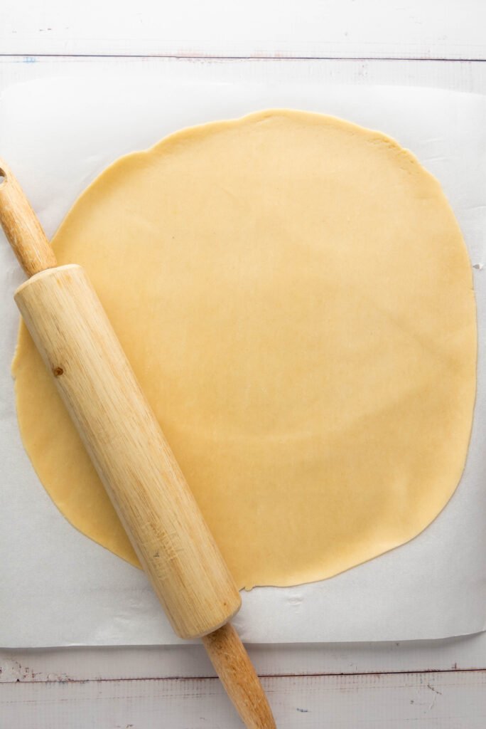 Pie dough rolled out flat on parchment paper with a wooden rolling pin