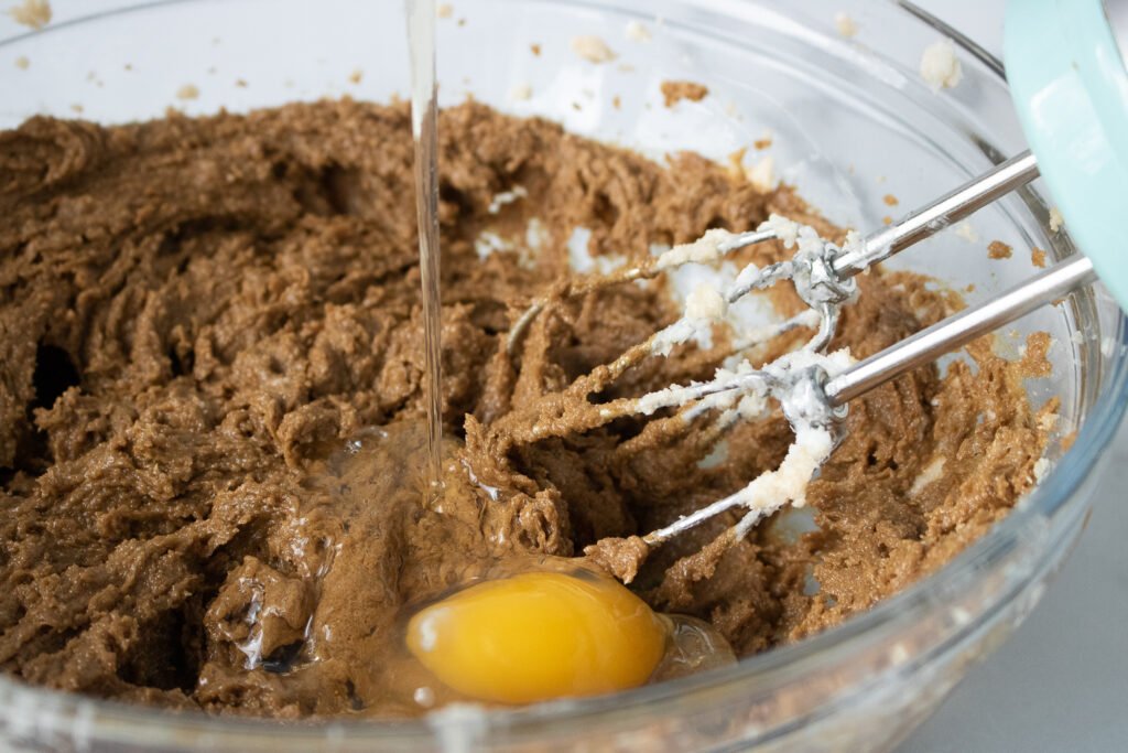 A cracked egg being added into the molasses cookie dough while mixing
