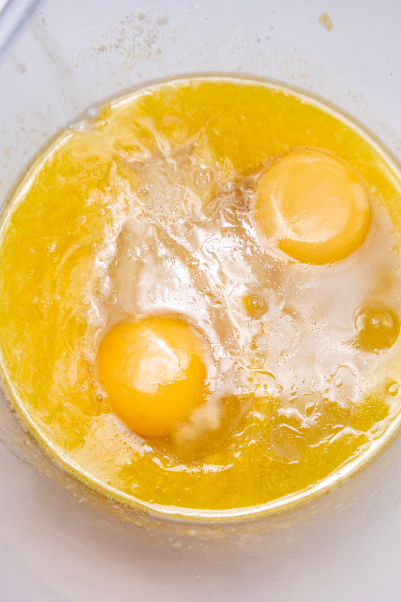 two eggs added to the butter and yeast mixture in a bowl, ready to be whisked into the dough base
