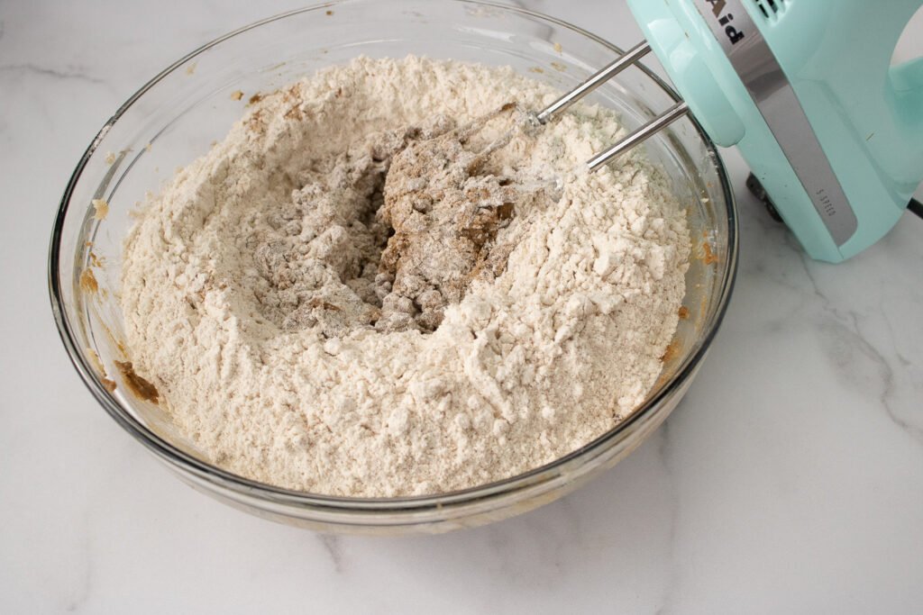 Flour and spices being added to the wet ingredients and ready to be mixed into cookie dough