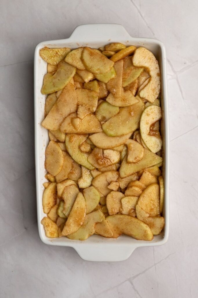 Prepared apple crisp filling spread evenly in a white baking dish before adding the topping