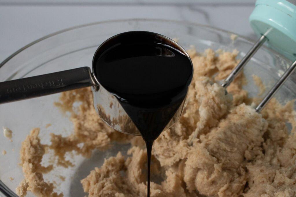 Molasses being poured into a bowl of creamed butter and sugar