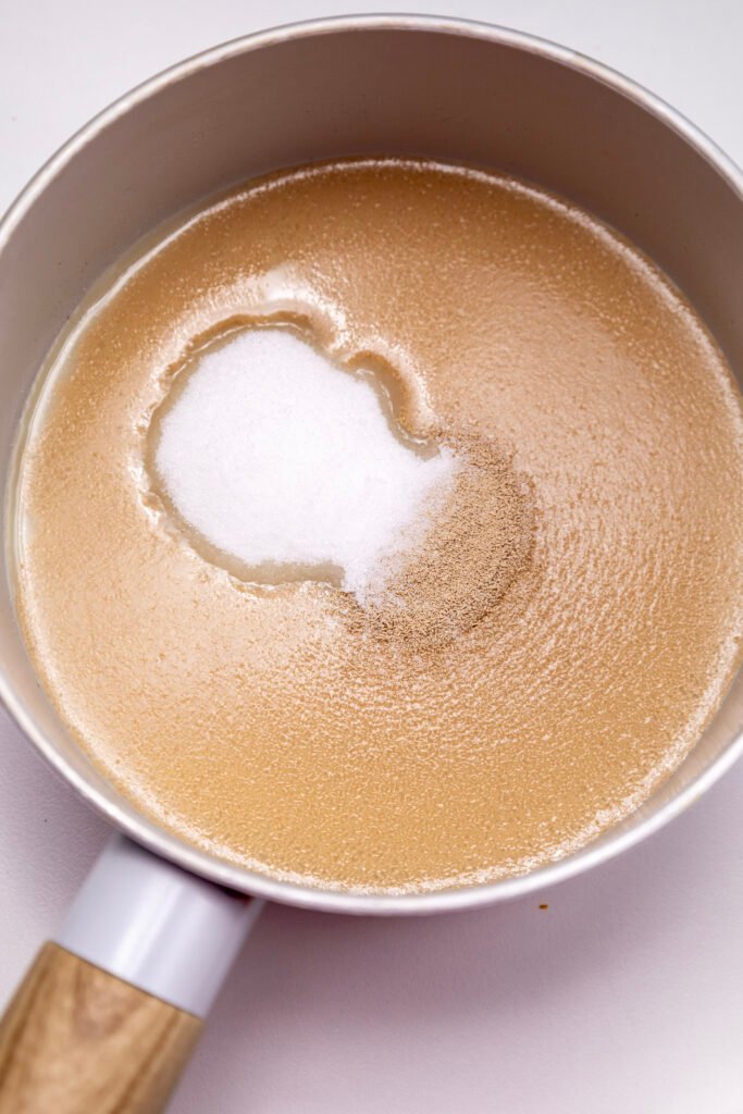 Dry yeast and sugar sprinkled over warm milk in a saucepan, just before mixing for proofing in the cinnamon roll dough