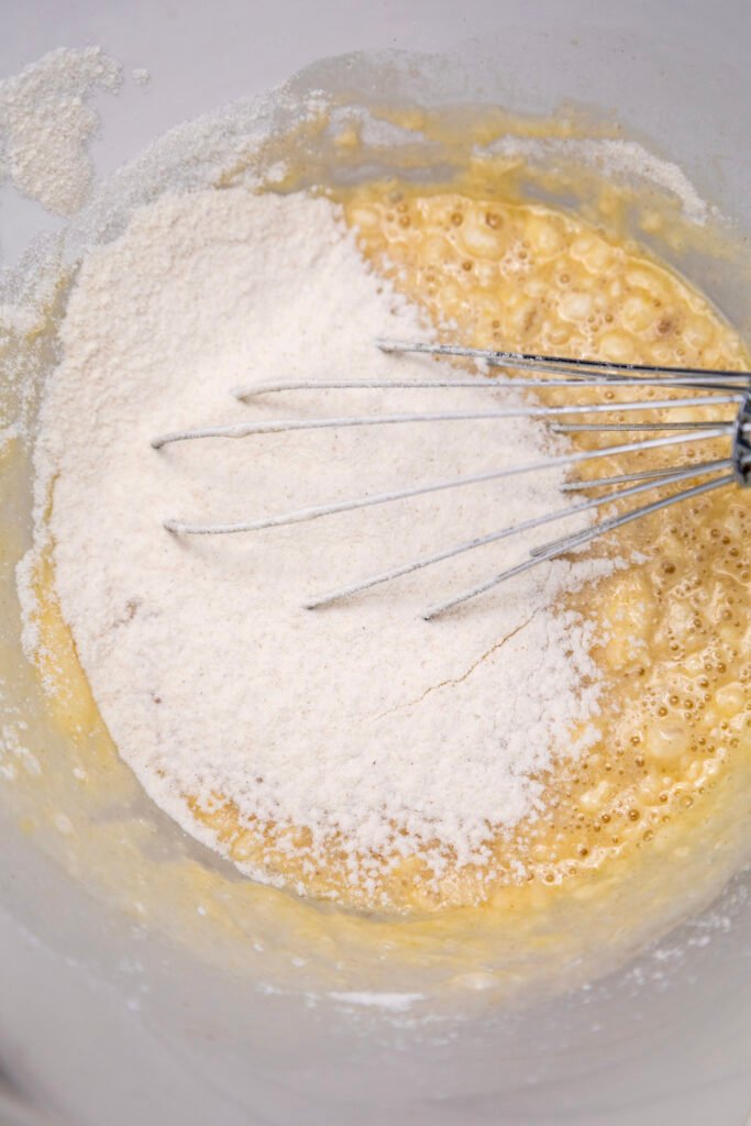 Flour added to the wet ingredients in a mixing bowl with a whisk