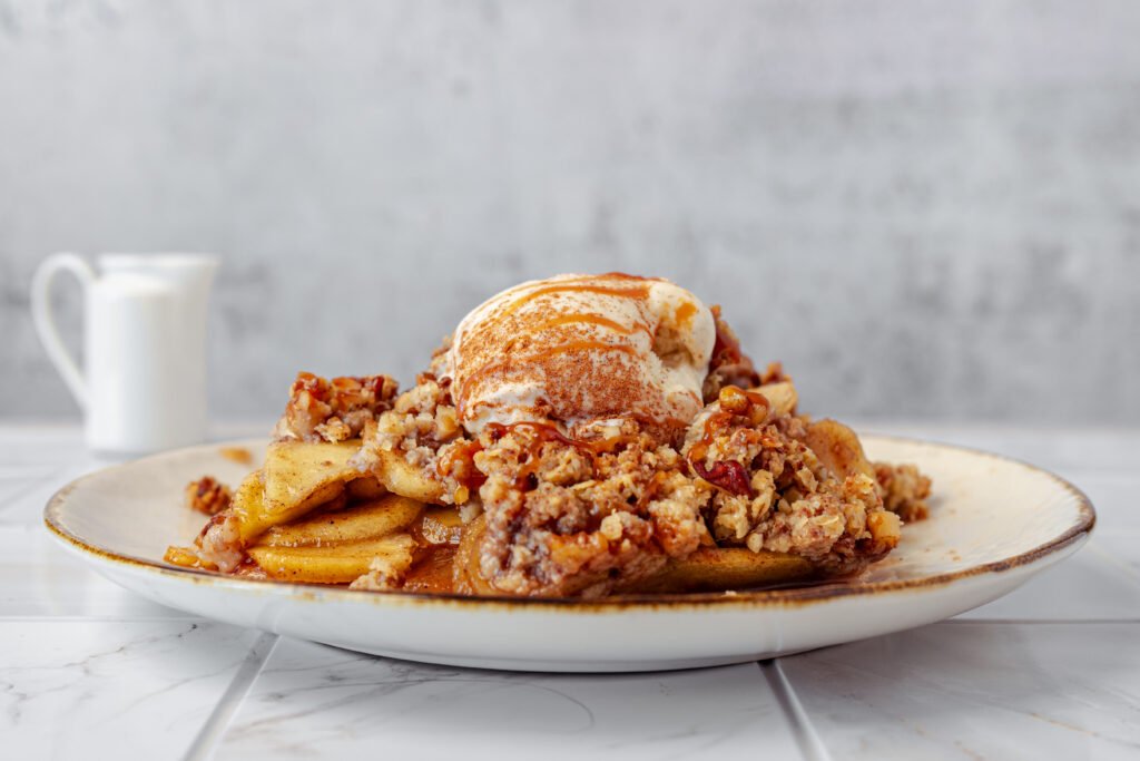 Plate of apple crisp topped with vanilla ice cream and caramel drizzle