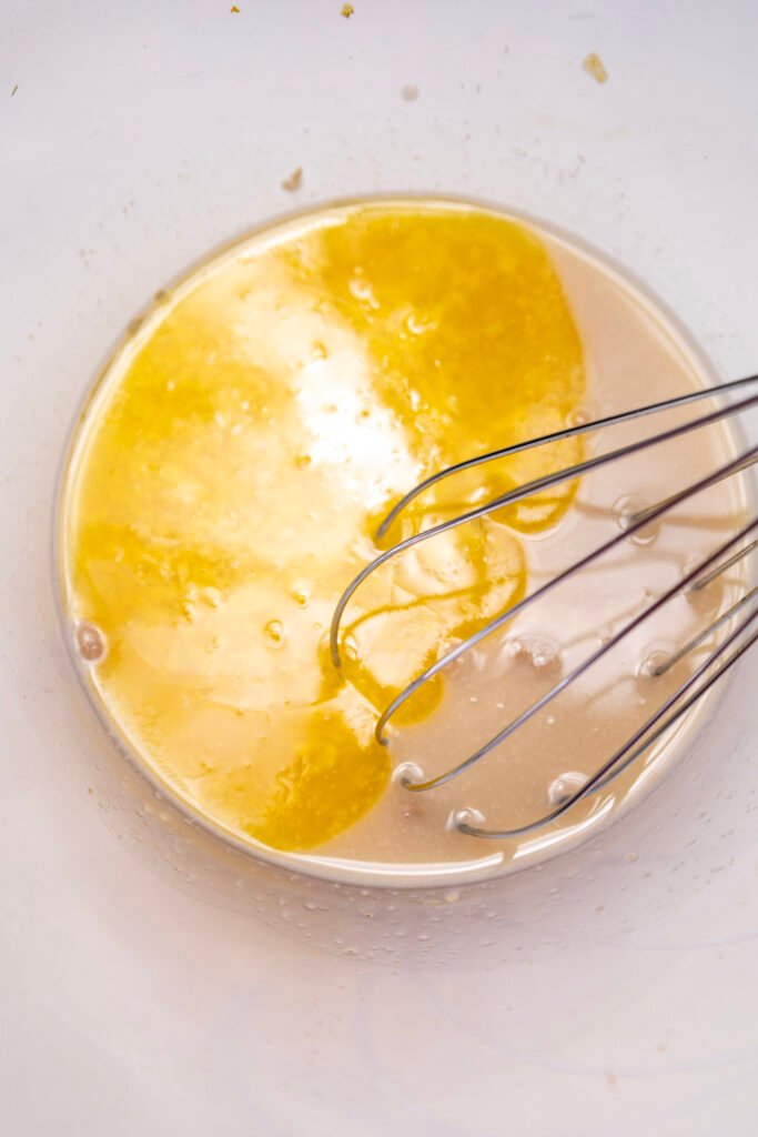 melted butter and proofed yeast mixture in a bowl with a whisk