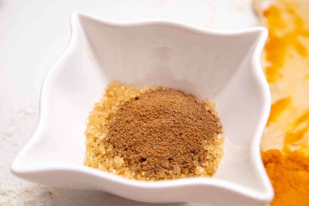 Close-up of a white bowl filled with brown sugar, cinnamon, and nutmeg, ready to be used as filling for pumpkin cinnamon rolls