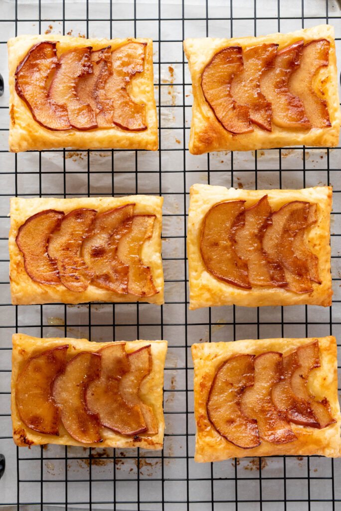 Upside down apple tarts cooling on a wire rack after being flipped, showing caramelized apple tops