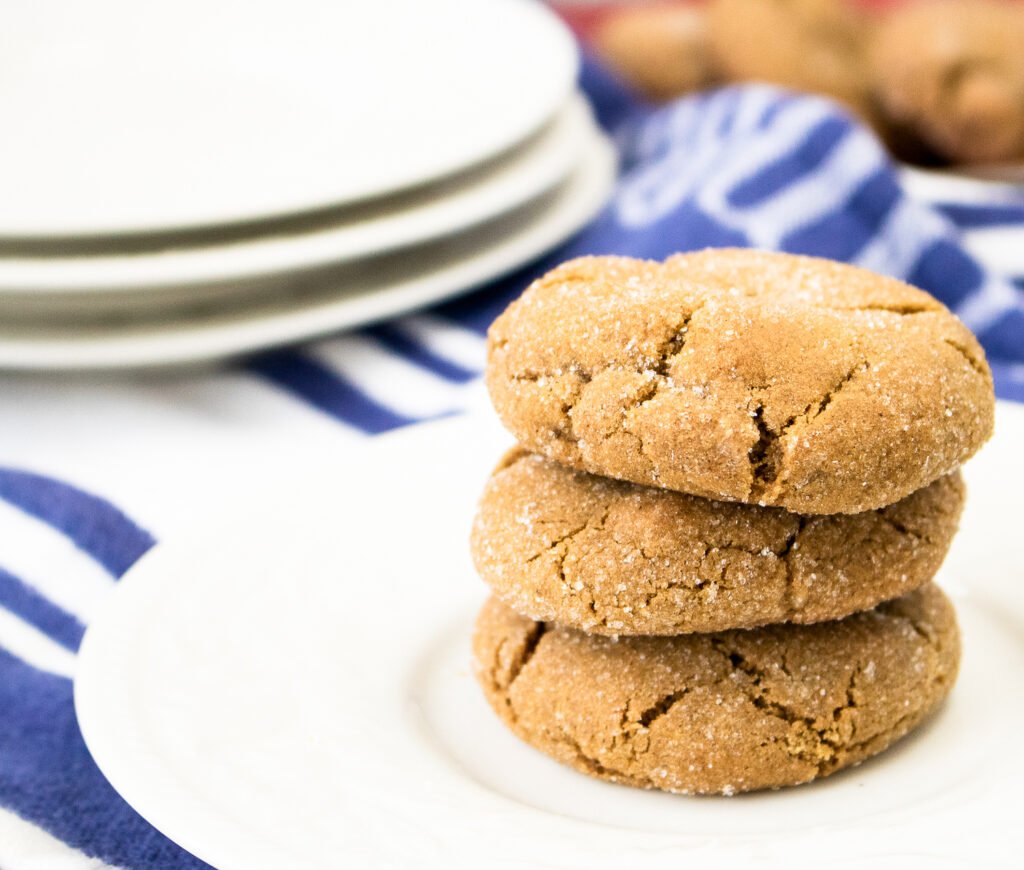 A stack of three chewy gingersnap cookies on a white plate
