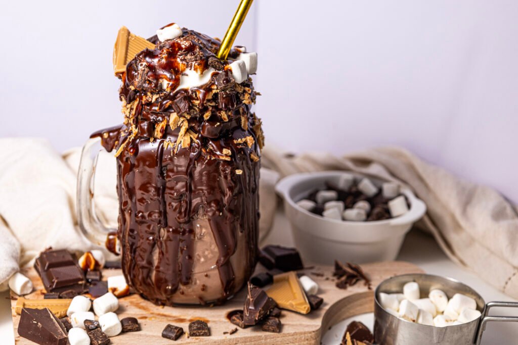 chocolate freakshake in a glass mug, dripping with melted chocolate and topped with whipped cream, marshmallows, chocolate chunks, and caramel pieces