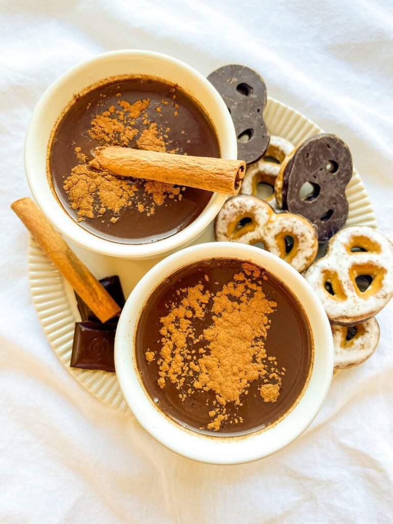 Two mugs of cinnamon tequila hot chocolate topped with ground cinnamon and a cinnamon stick