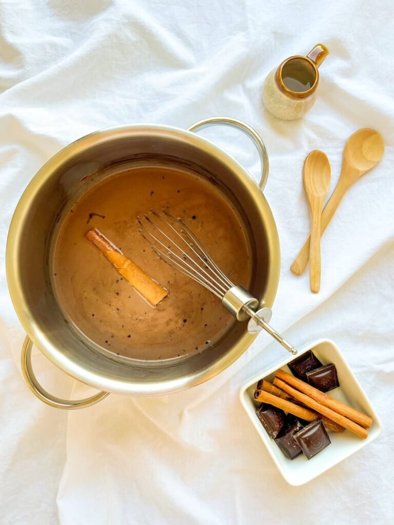 Cinnamon stick simmering in a saucepan of cinnamon tequila hot chocolate with a whisk
