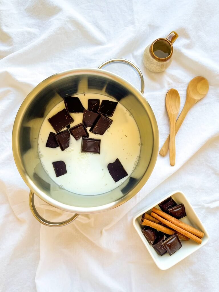 Dark chocolate squares melting in warm milk inside a saucepan

