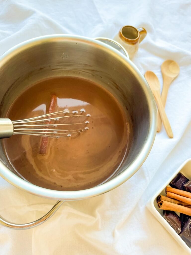 Cinnamon stick simmering in a saucepan of cinnamon tequila hot chocolate with a whisk
