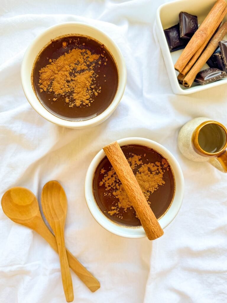 Two mugs of cinnamon tequila hot chocolate topped with ground cinnamon and a cinnamon stick