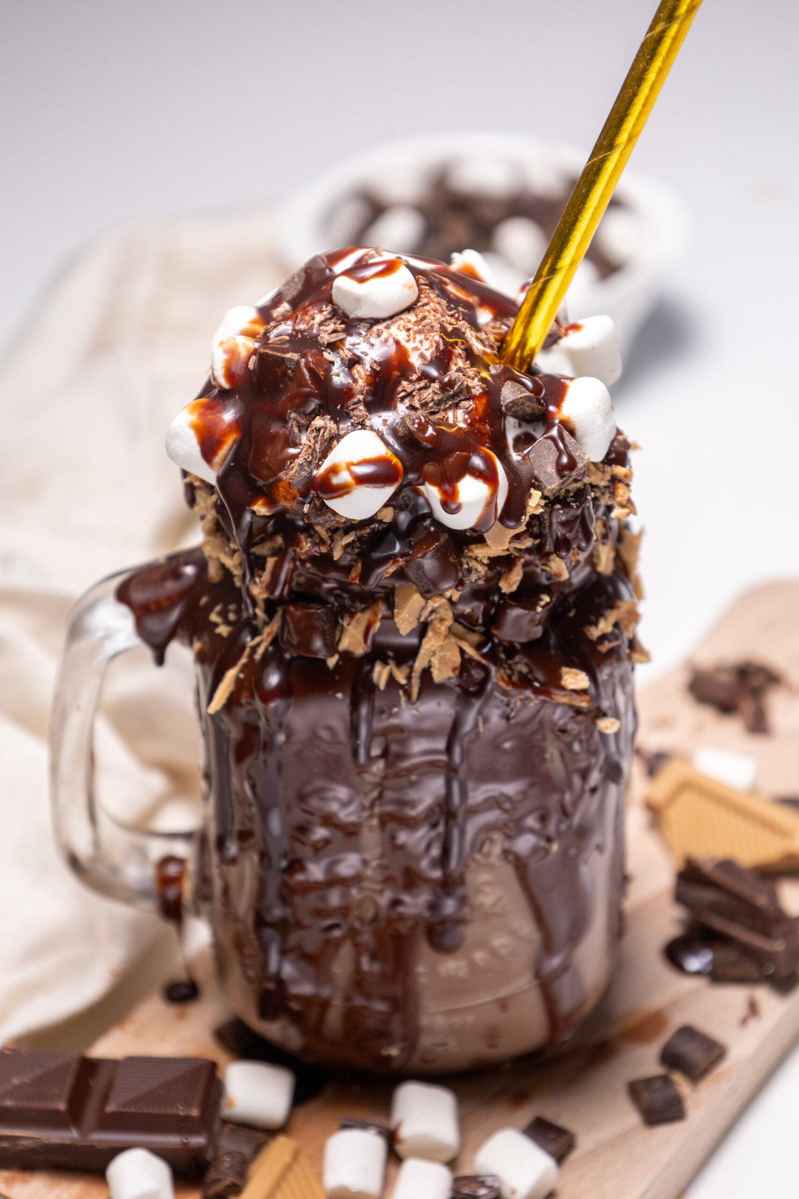 chocolate freakshake in a glass mug, dripping with melted chocolate and topped with whipped cream, marshmallows, chocolate chunks, and caramel pieces