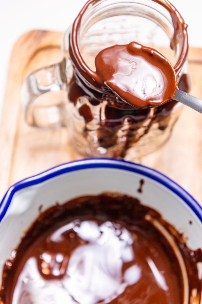 A spoon spreading melted chocolate around the rim of a tall glass mug
