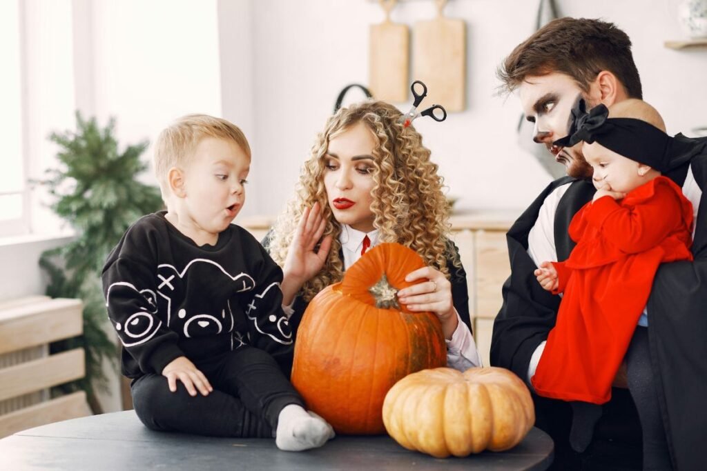 A family in Halloween costumes gathers around a table with pumpkins