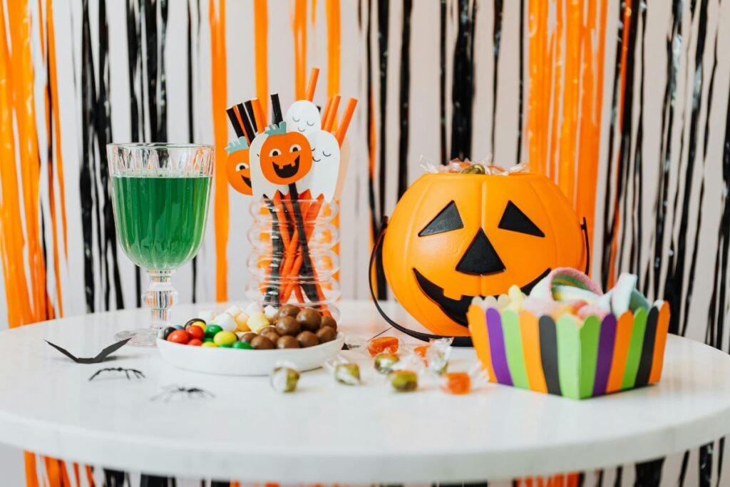 Halloween party table decorated with orange and black streamers, featuring a green drink in a glass and candies