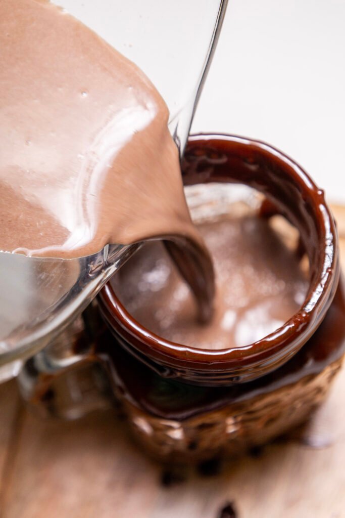 Blended chocolate freakshake being poured from a blender into a glass coated with melted chocolate