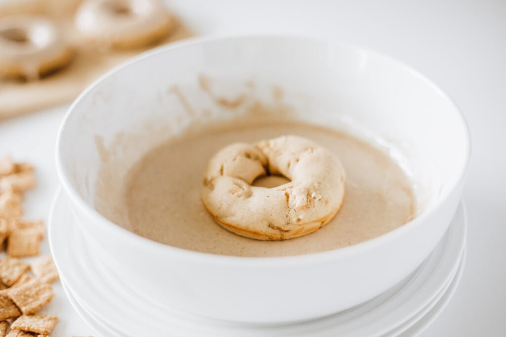 Baked Cinnamon Toast Crunch Donut being dipped into a bowl of smooth maple glaze