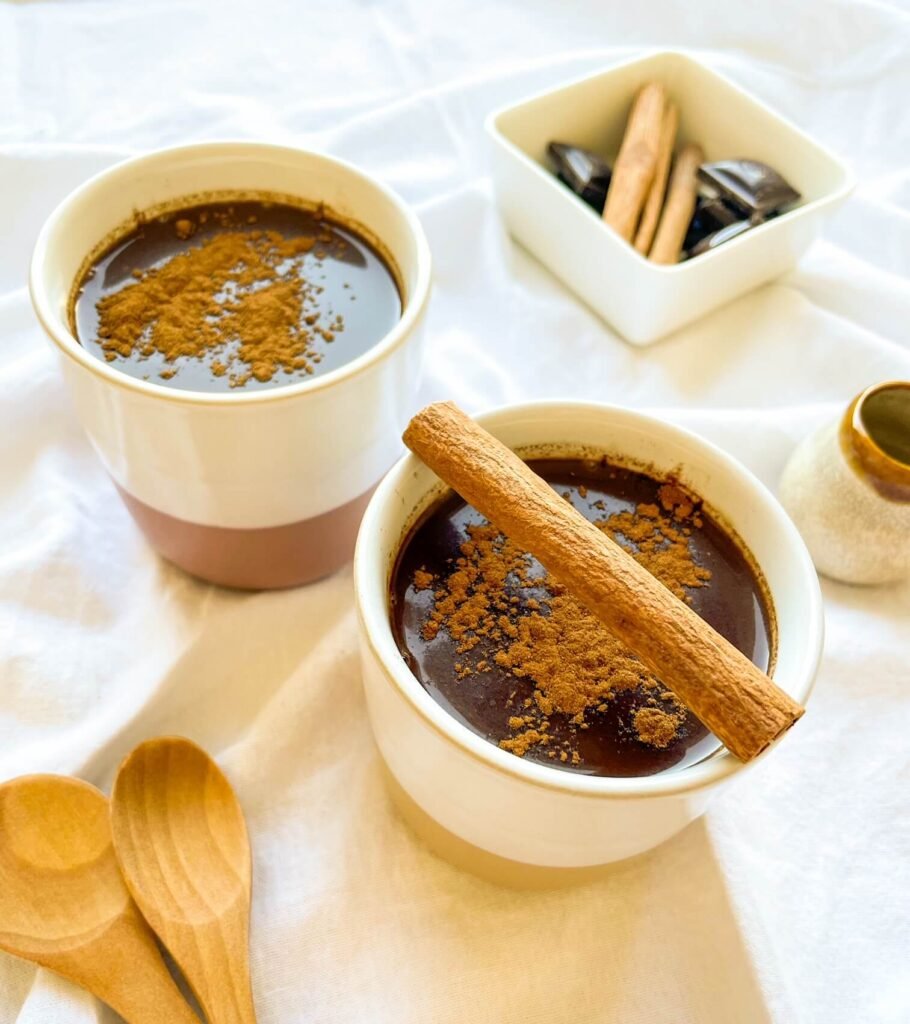 Two mugs of cinnamon tequila hot chocolate topped with ground cinnamon and a cinnamon stick